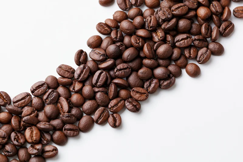 Roasted coffee beans scattered across white surface with copyspace