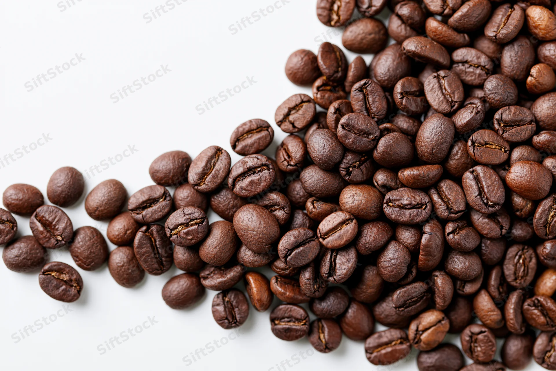 Roasted coffee beans scattered and falling across a white surface in a top-down view