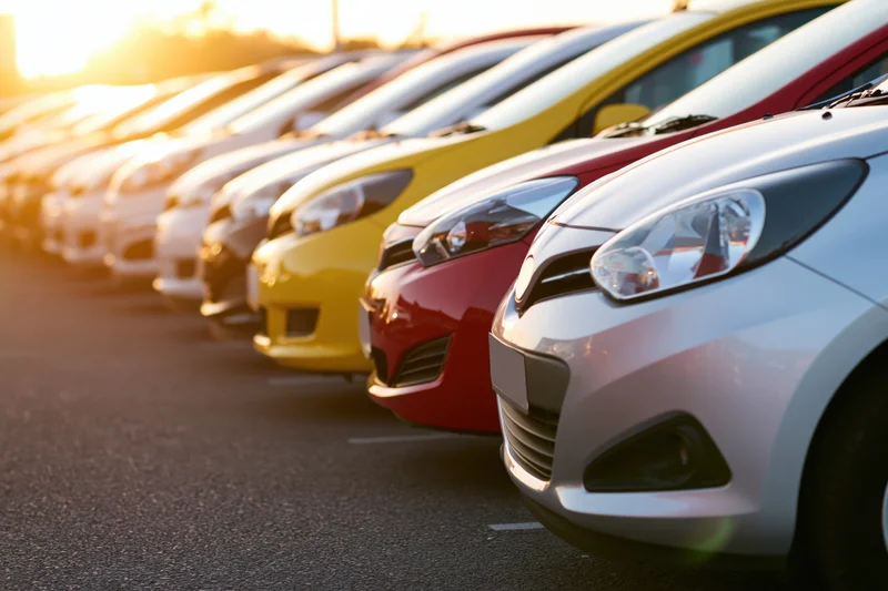 Row of compact cars parked side by side in a dealership lot at golden hour
