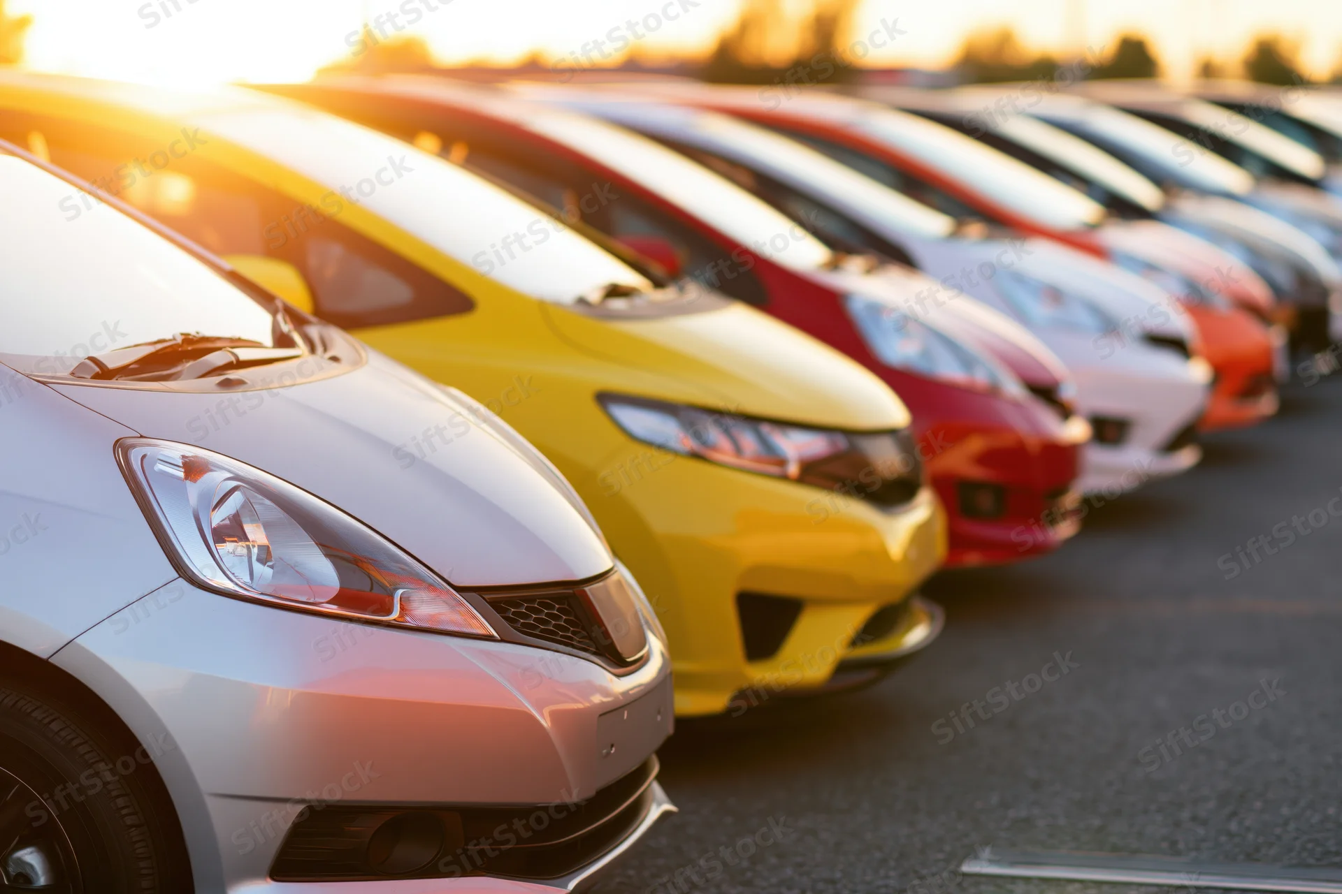 Row of compact cars parked side by side in a dealership lot at sunset