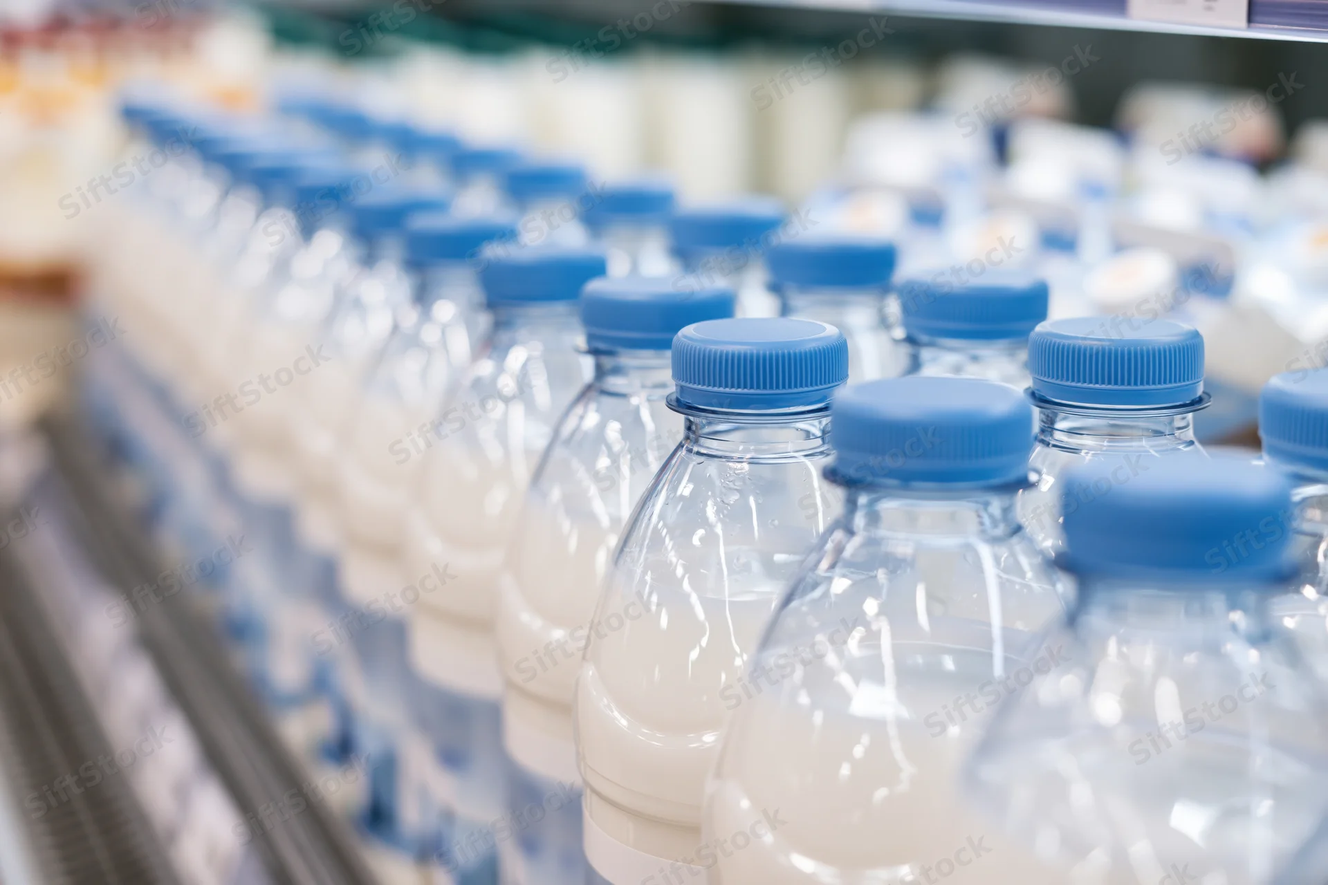 Rows of clear plastic milk bottles with blue caps lined up on a supermarket shelf
