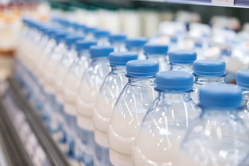 Rows of clear plastic milk bottles with blue caps lined up on a supermarket shelf