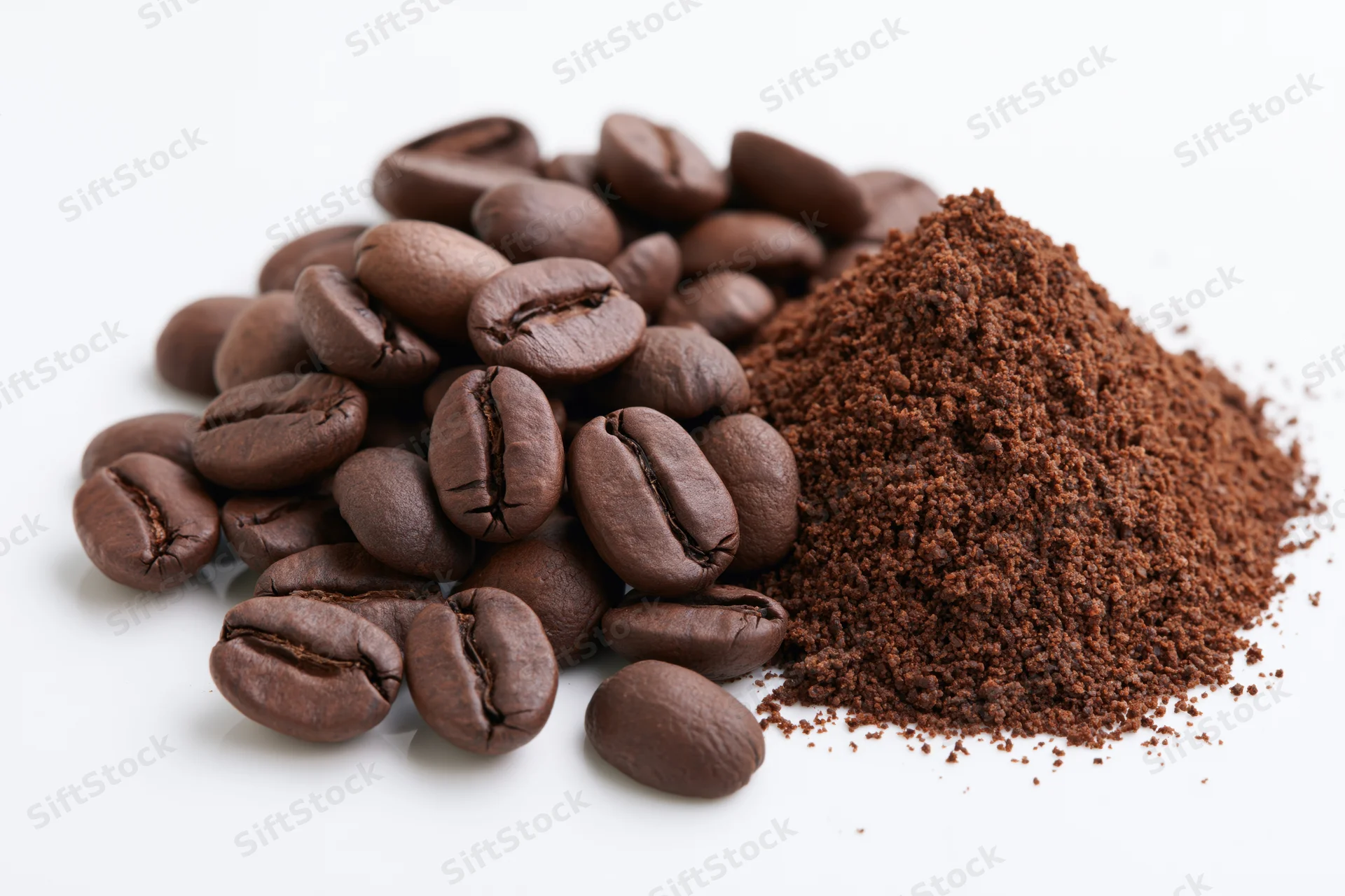 Whole roasted coffee beans and ground coffee piled together on a white surface