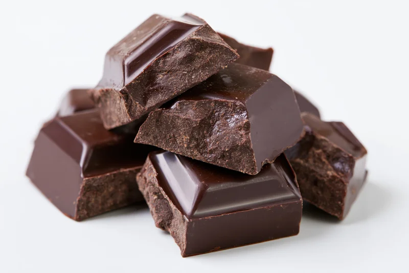 Broken dark chocolate chunks stacked loosely on white background