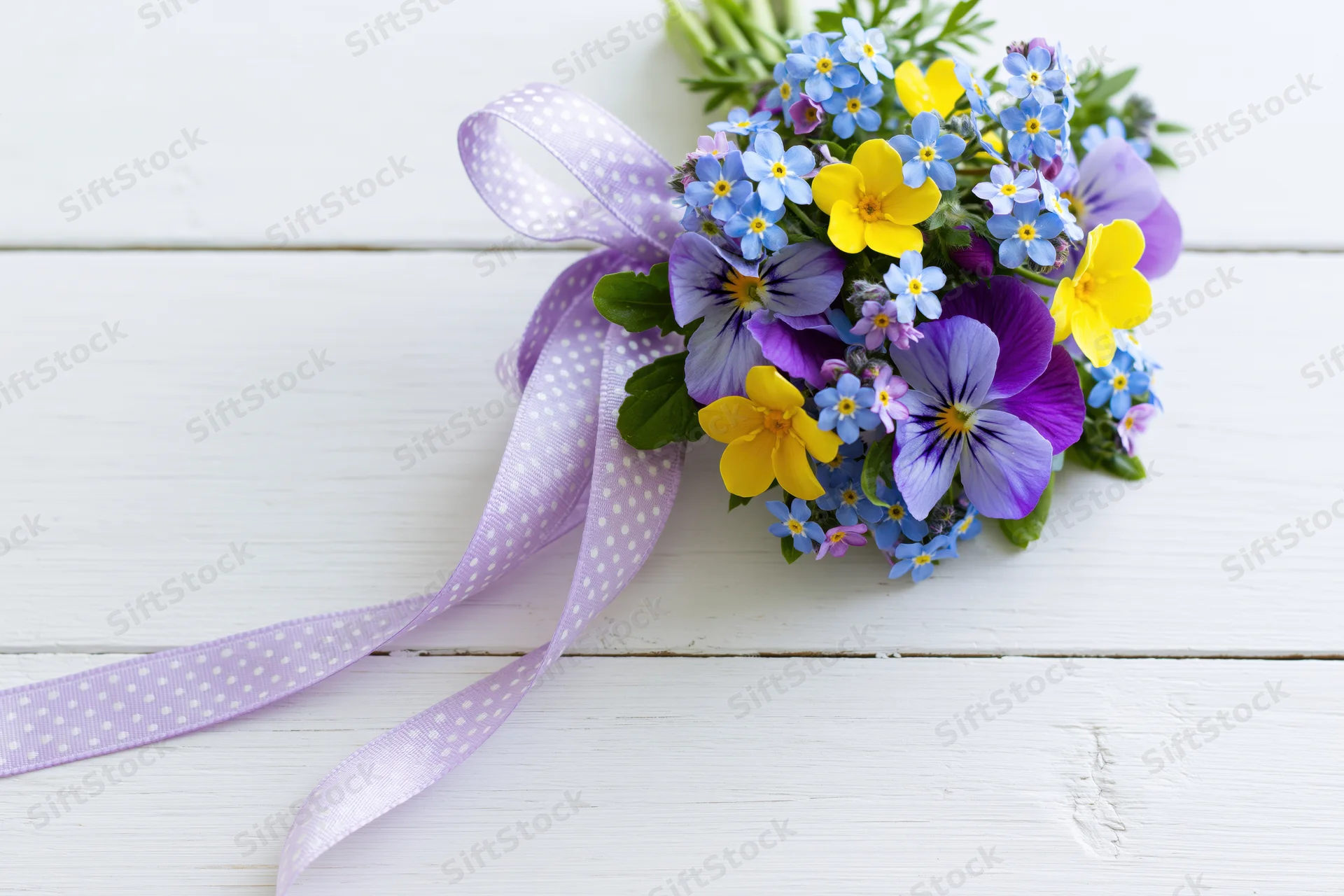 Small bouquet of forget-me-nots and viola pansies tied with a purple polka dot ribbon on a white wooden surface