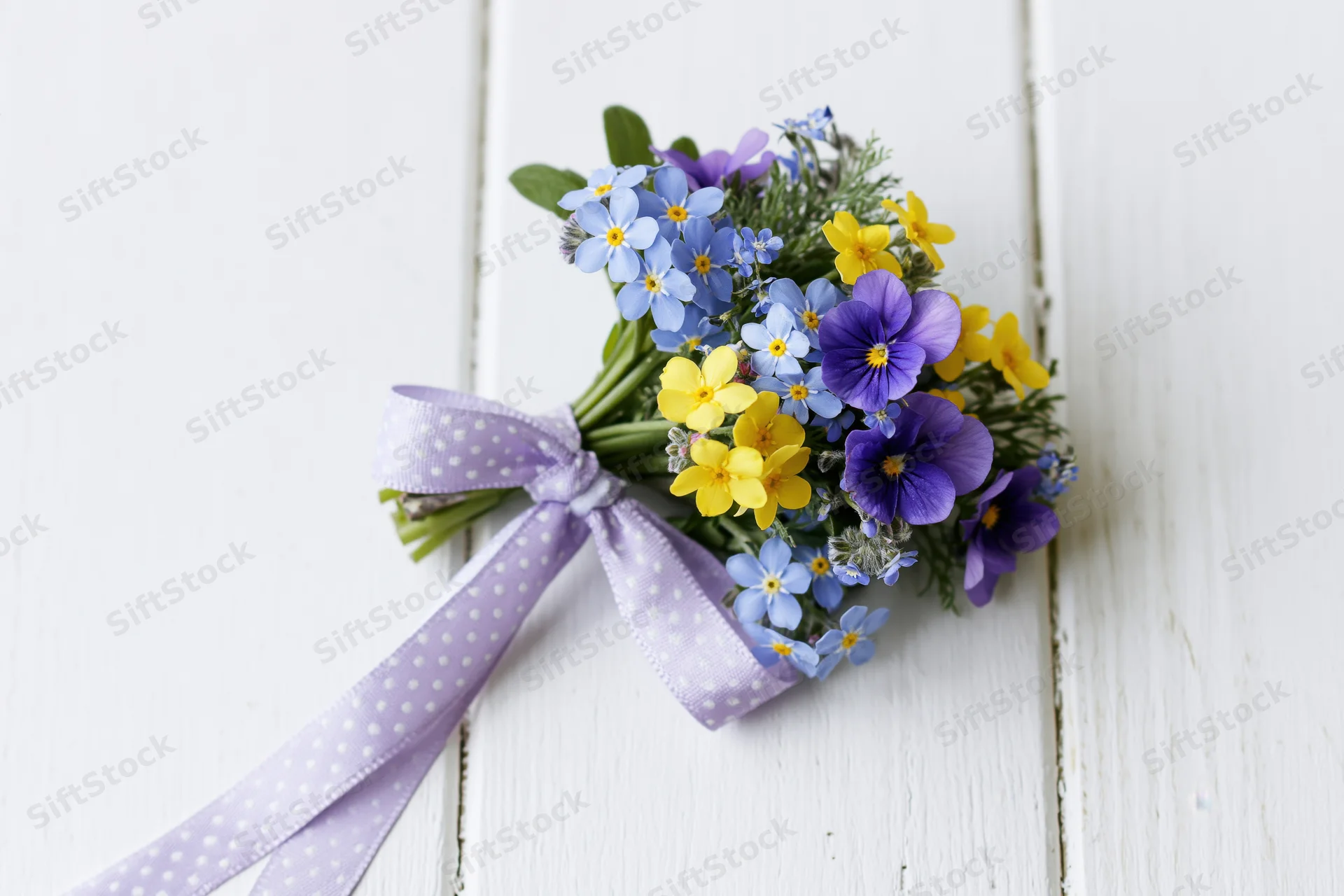 Small bouquet of forget-me-nots and viola pansies tied with lavender polka dot ribbon on white wooden surface