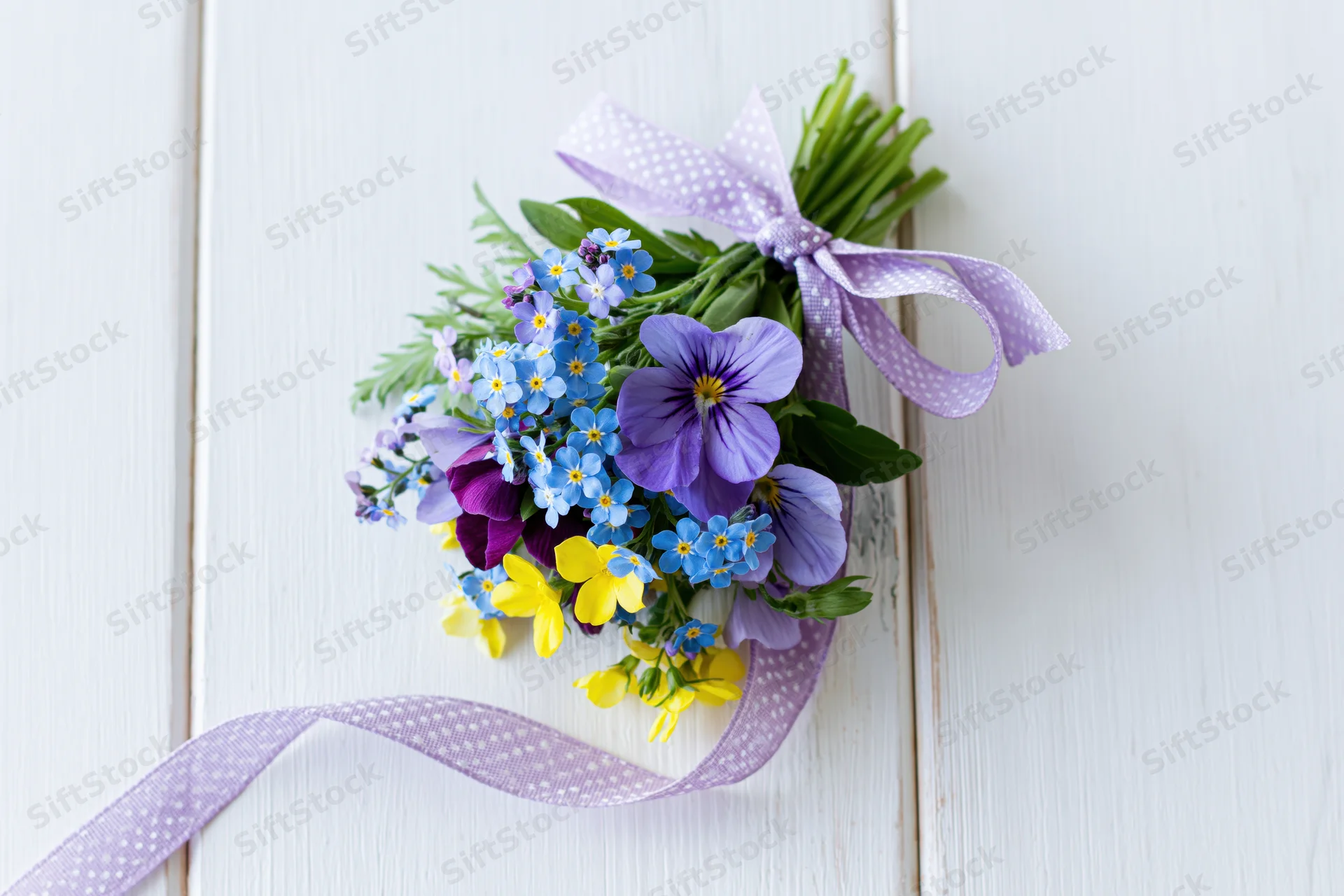 Small bouquet of forget-me-nots and viola pansies tied with purple ribbon on white wooden surface
