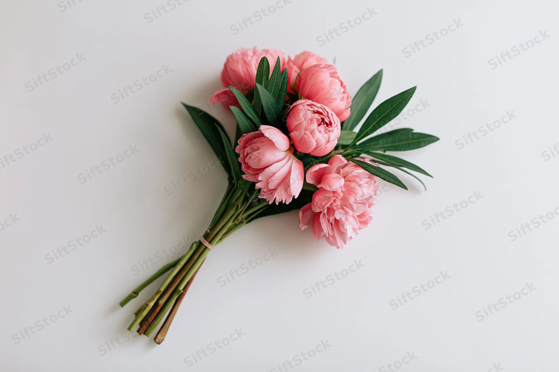 Small bouquet of pink peonies with green leaves laid flat on white surface