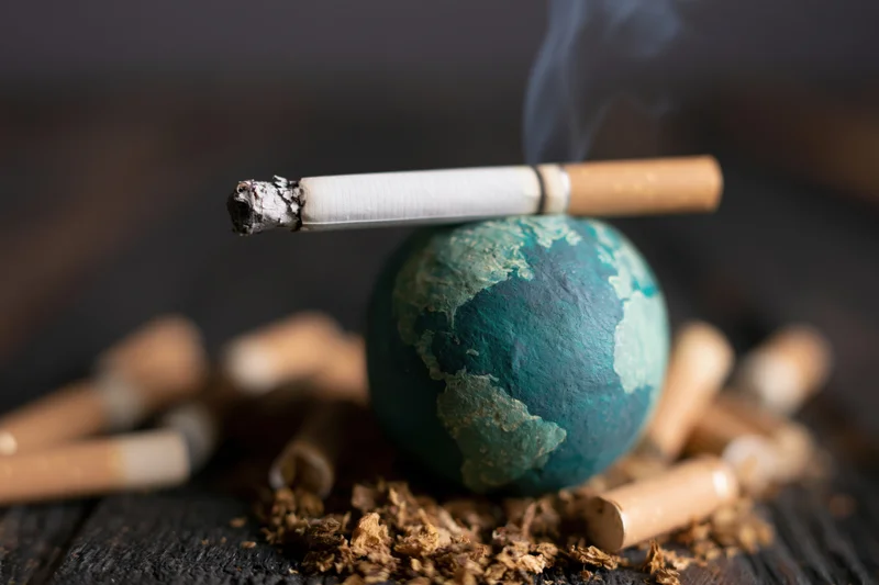 Lit cigarette resting on a painted globe surrounded by cigarette butts and ash on a wooden surface