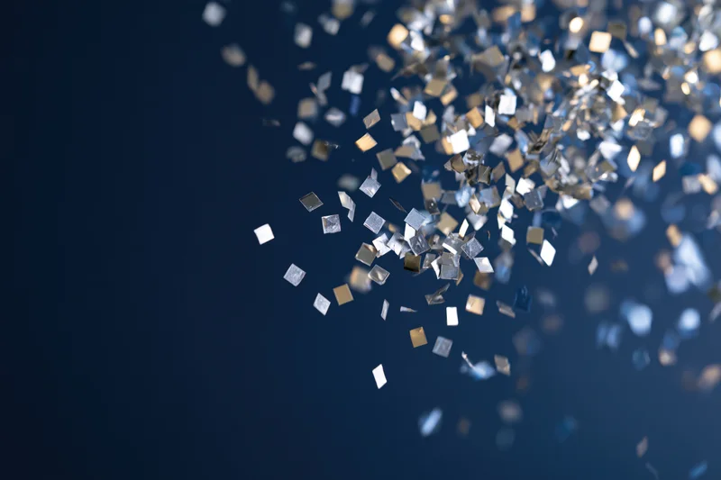 Metallic confetti pieces floating midair against a dark blue background with copyspace on the left