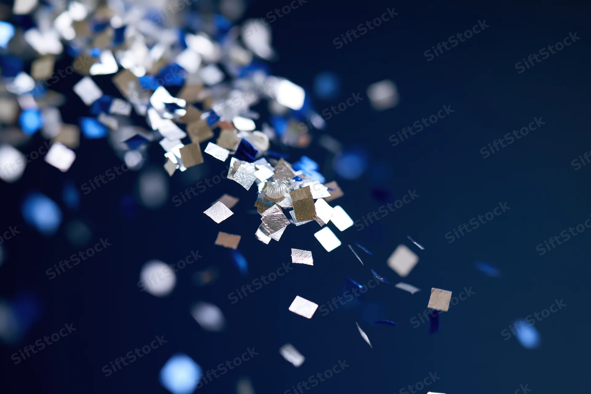 Metallic confetti pieces falling in mid-air against a dark blue background with bokeh highlights