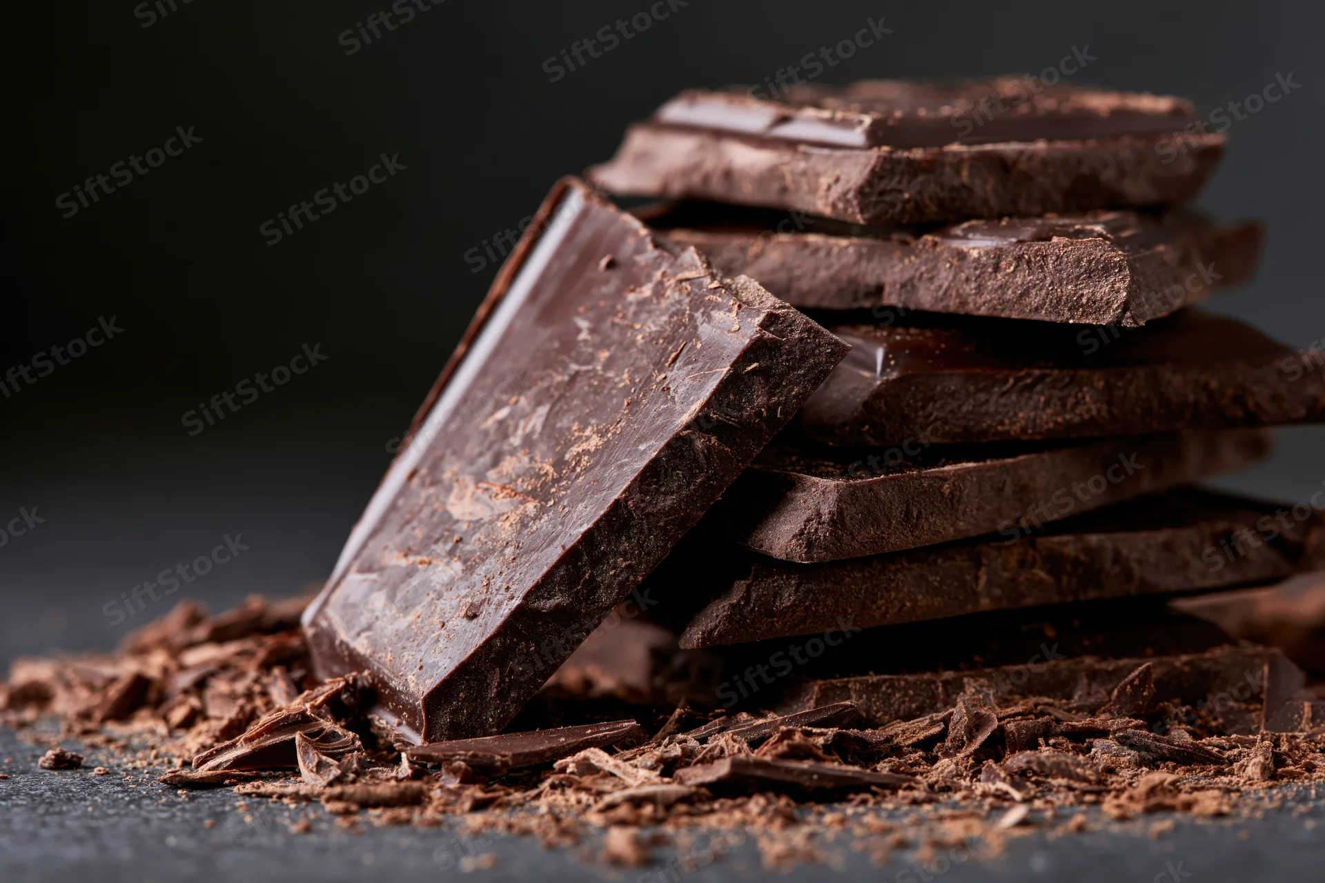 Broken dark chocolate slabs stacked on a dark surface with scattered crumbs