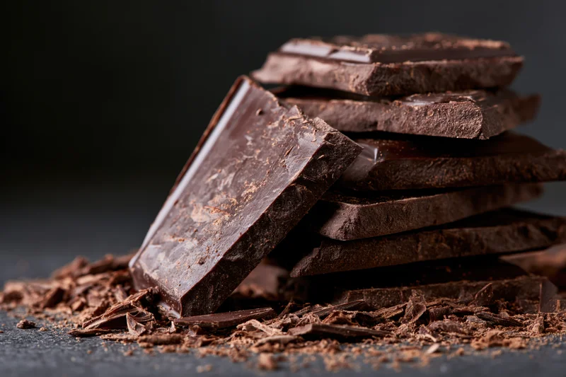 Broken dark chocolate slabs stacked on a dark surface with scattered crumbs