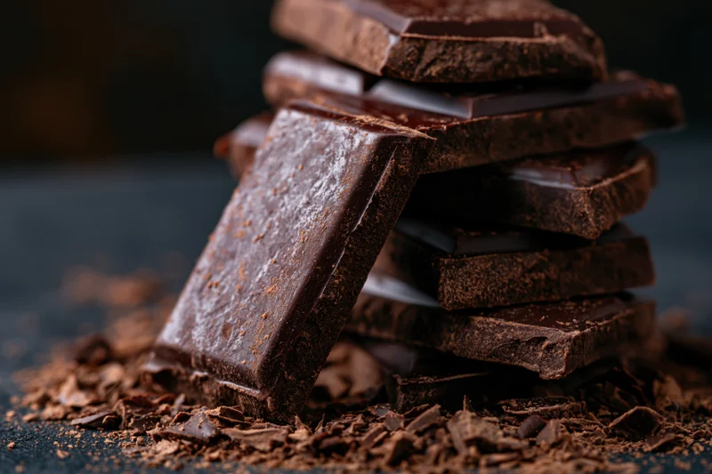Broken dark chocolate slabs stacked on a dark surface with crumbs scattered around
