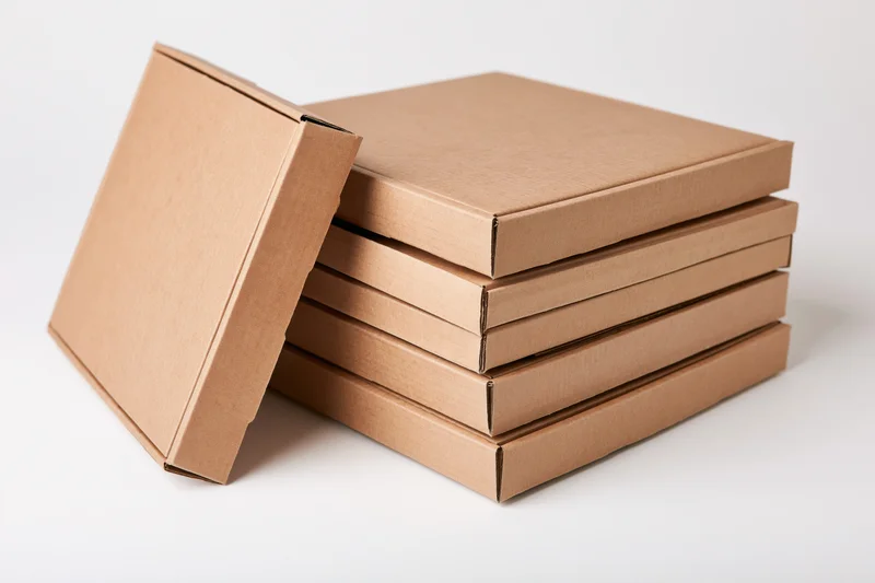 Stack of five plain cardboard pizza boxes with one leaning against the pile on white background