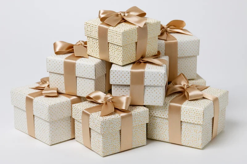 Stack of seven white gift boxes with gold polka dots and satin ribbons arranged in pyramid formation on white background