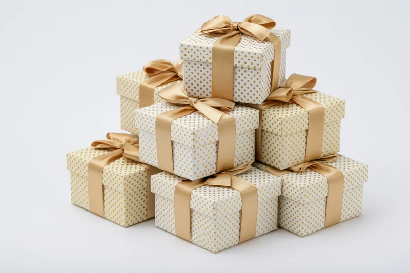 Stack of seven white gift boxes with gold polka dots and satin ribbons arranged in pyramid shape on white background