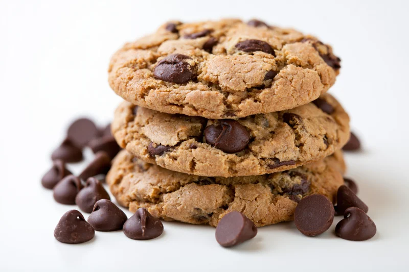 Stack of three homemade chocolate chip cookies piled together on white surface