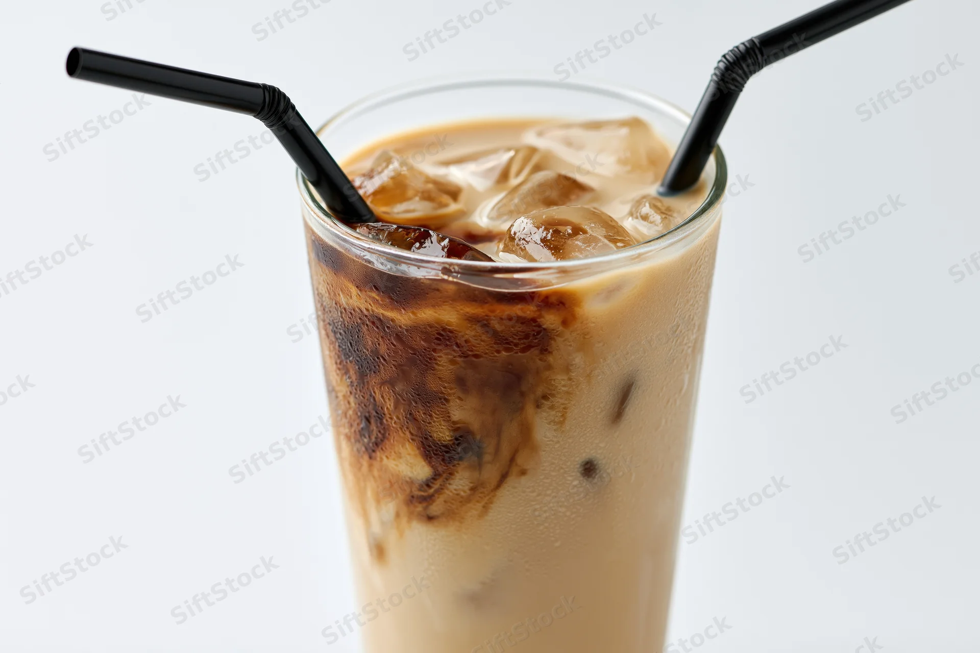 Tall glass of iced coffee with milk and ice cubes, two black straws, on white background