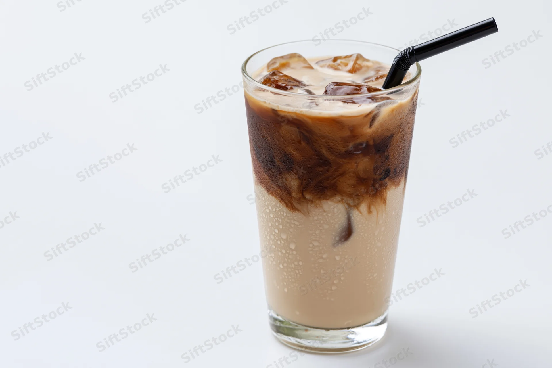 Tall glass of iced coffee with milk and ice cubes, black straw, condensation on surface, white background