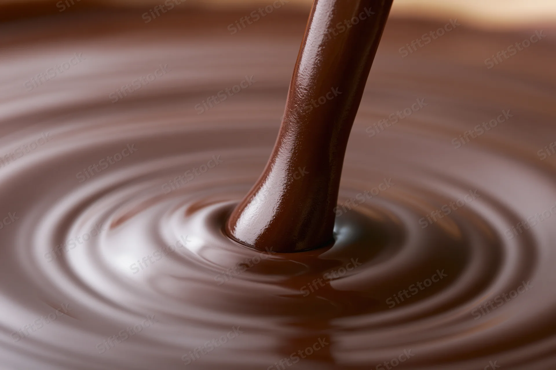 Thick stream of melted dark chocolate pouring into a pool creating ripples