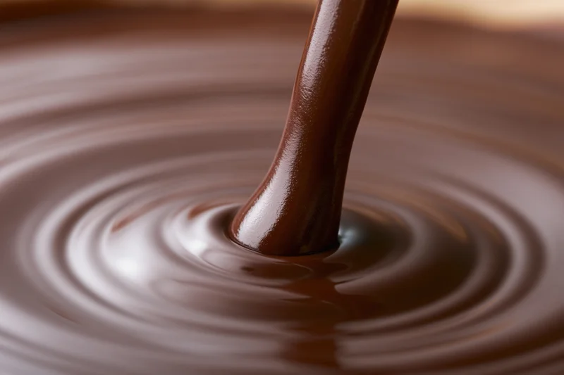 Thick stream of melted dark chocolate pouring into a pool creating ripples