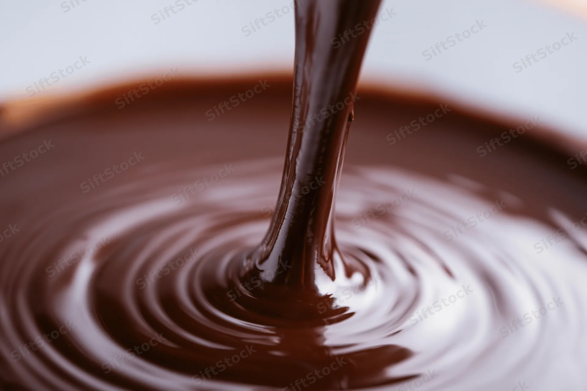 Thick stream of melted dark chocolate pouring into a pool creating ripples