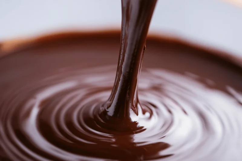 Thick stream of melted dark chocolate pouring into a pool creating ripples