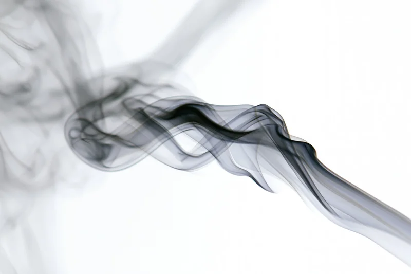Dark smoke curling upward in thin wisps against a white background