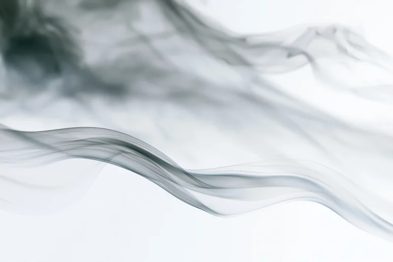 Thin wisps of dark smoke curling and drifting upward against a white background