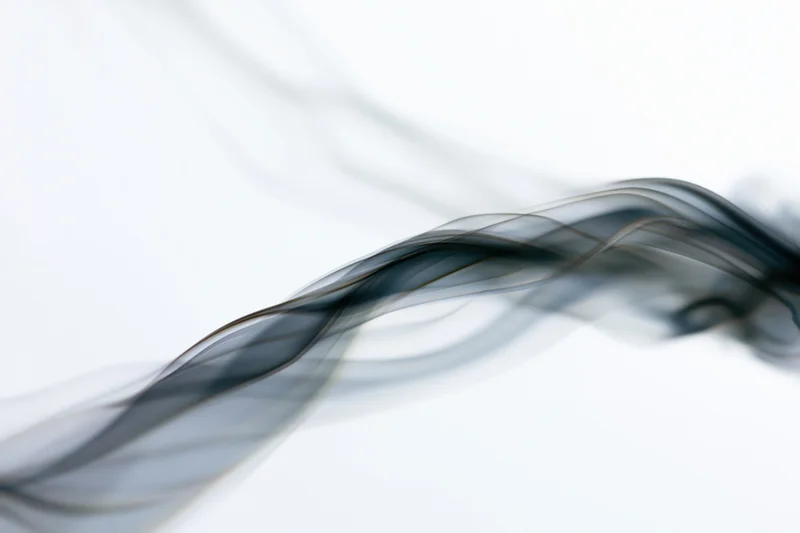 Dark smoke wisps curling and drifting upward against a white background