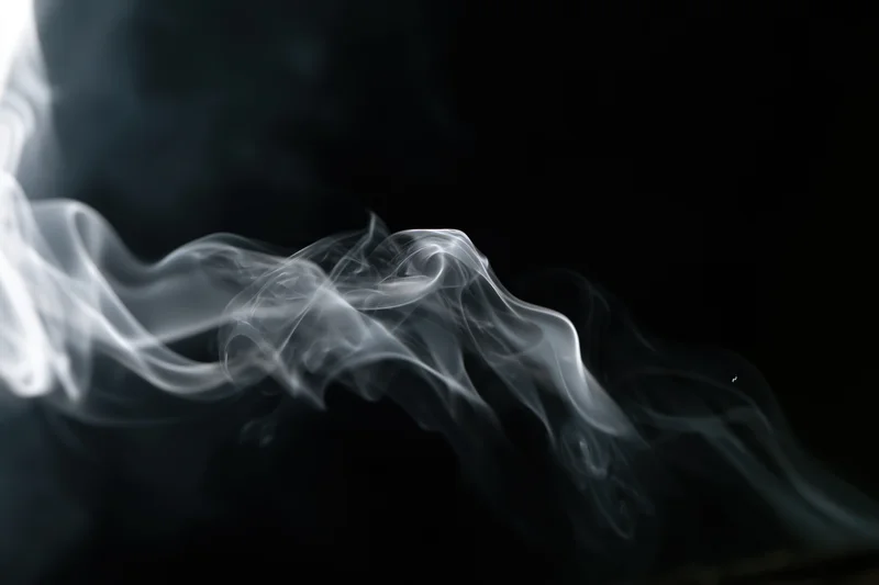 White smoke curling and drifting upward against a black background