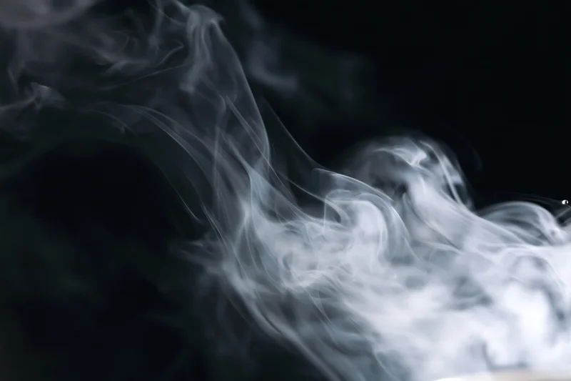 White smoke curling and drifting upward against a black background