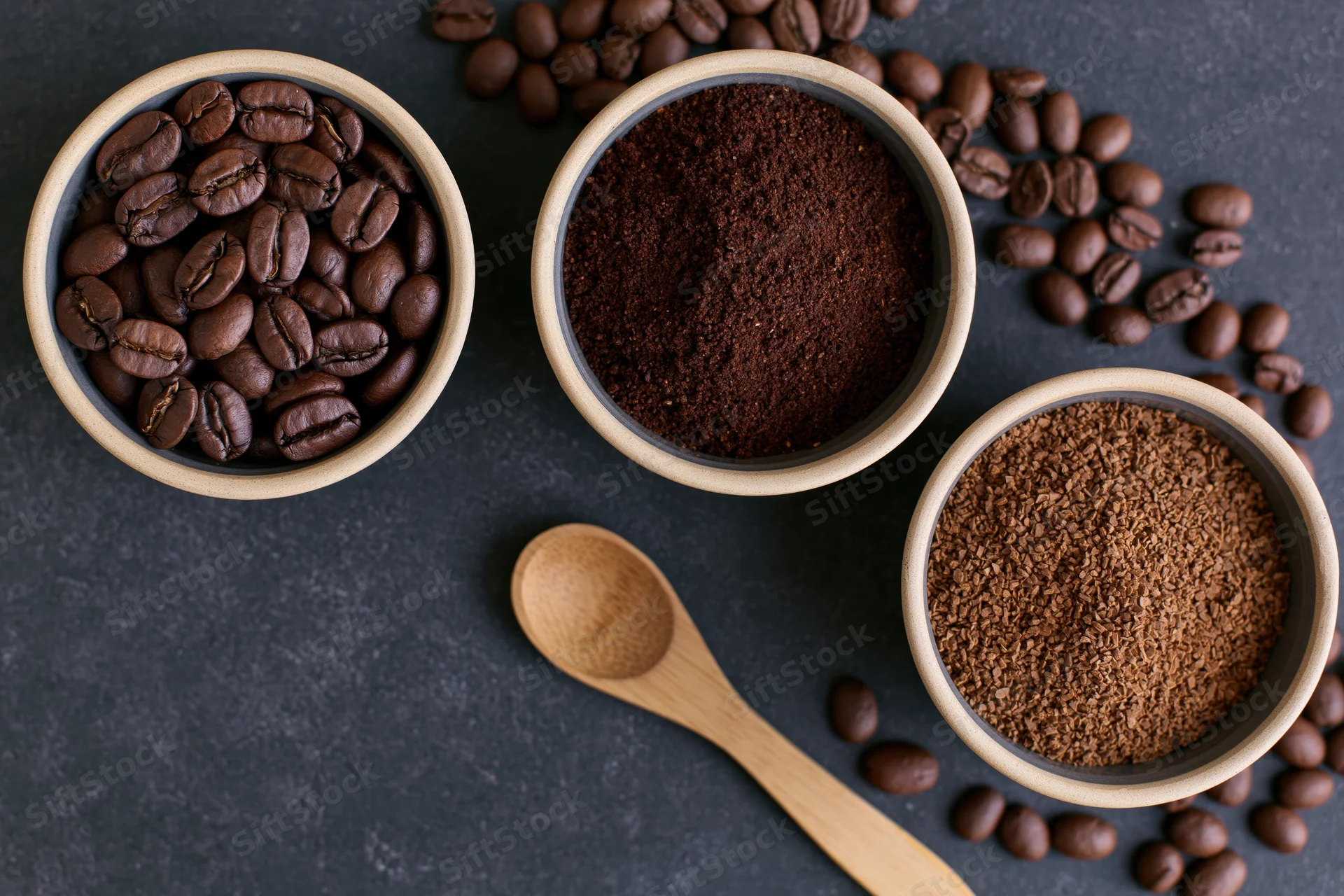 Three bowls with coffee beans, ground coffee and instant coffee arranged on dark surface with wooden spoon