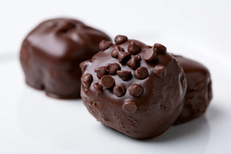 Three dark chocolate-coated candies clustered together on a white surface