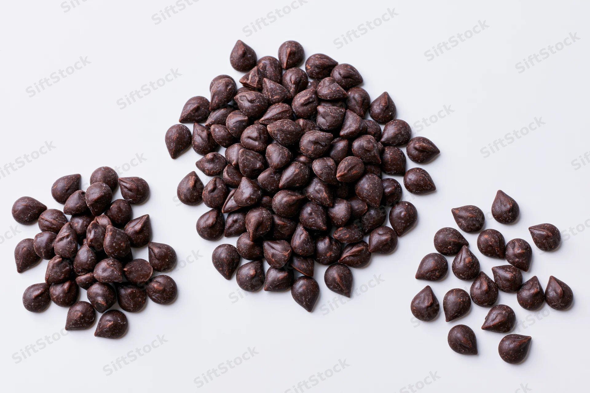 Three piles of dark chocolate chips scattered on a plain white surface