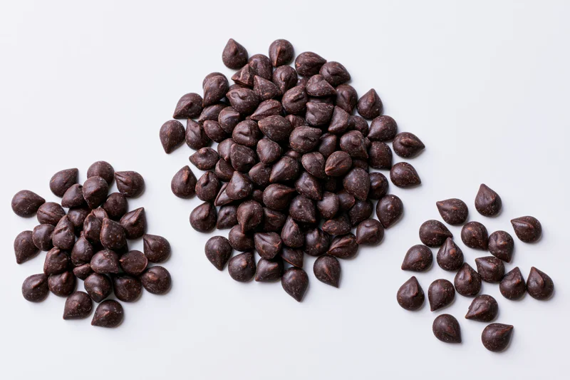 Three piles of dark chocolate chips scattered on a plain white surface