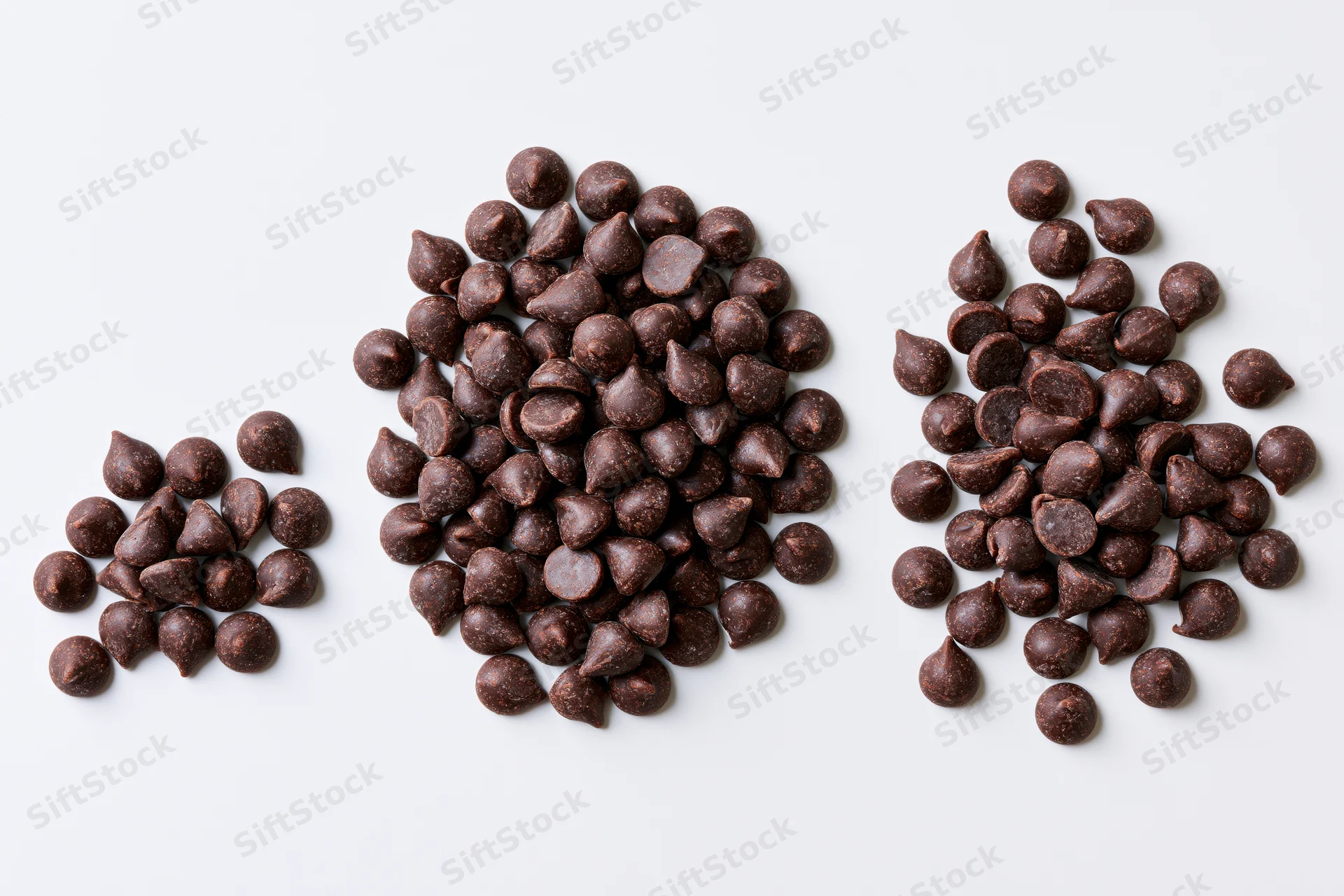 Three piles of dark chocolate chips arranged on a plain white surface