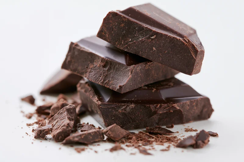 Broken dark chocolate pieces stacked loosely on white background
