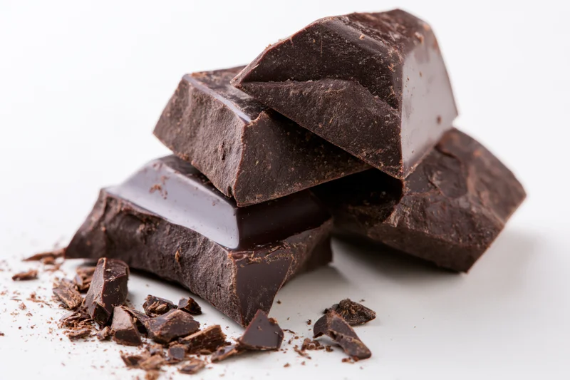 Broken dark chocolate pieces stacked loosely on white background