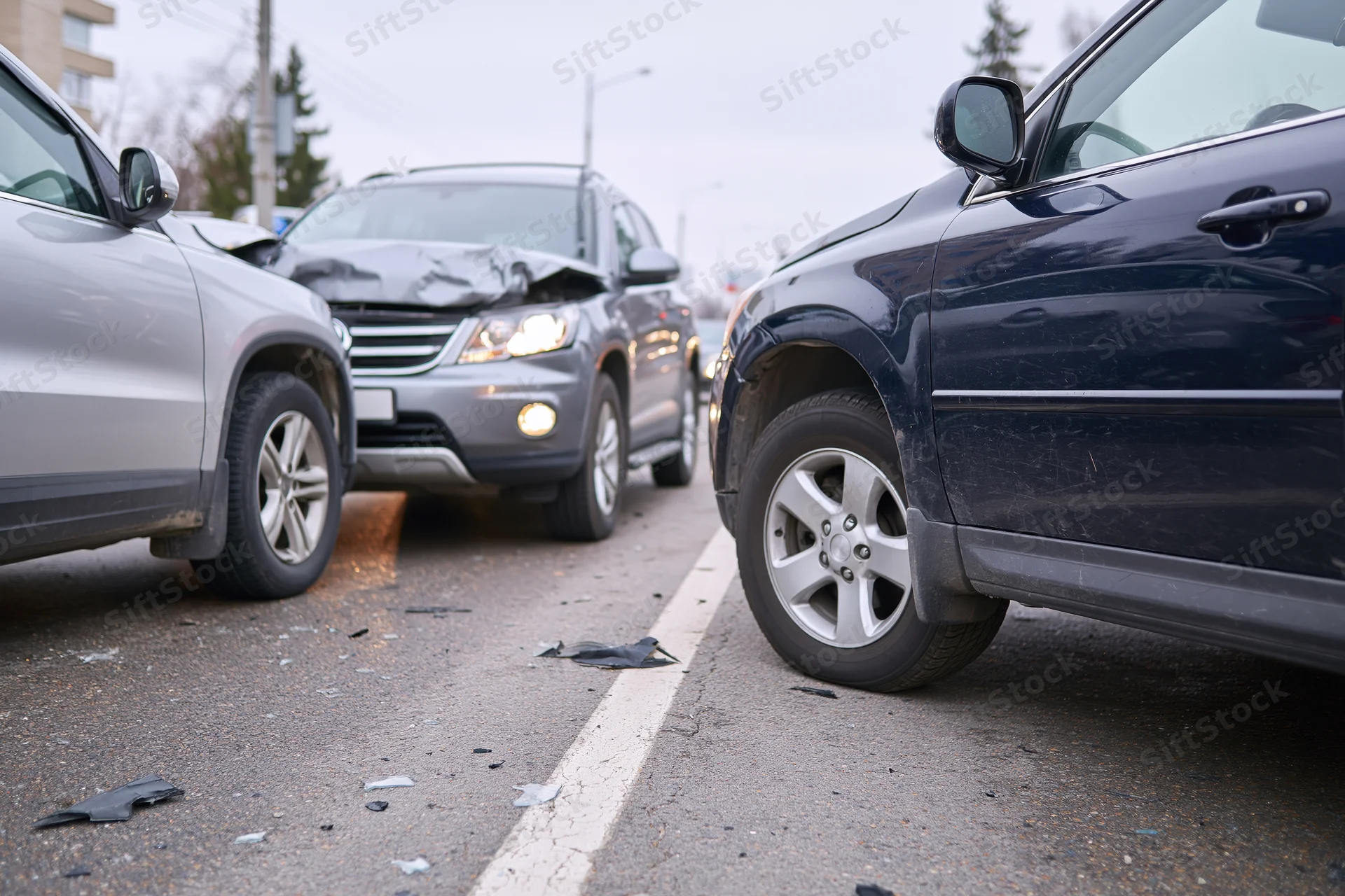 Three suvs involved in a front-end collision on an urban road with visible damage and debris on the pavement