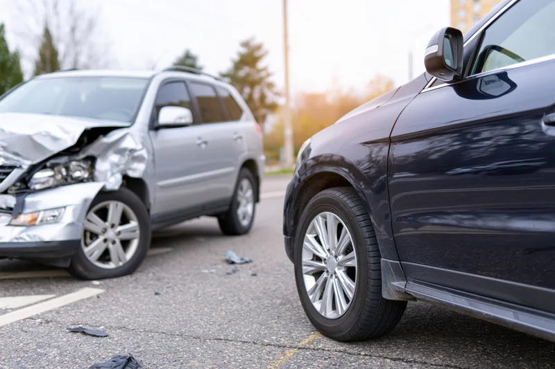 Two suvs after front-end collision on urban road with visible damage and debris on asphalt