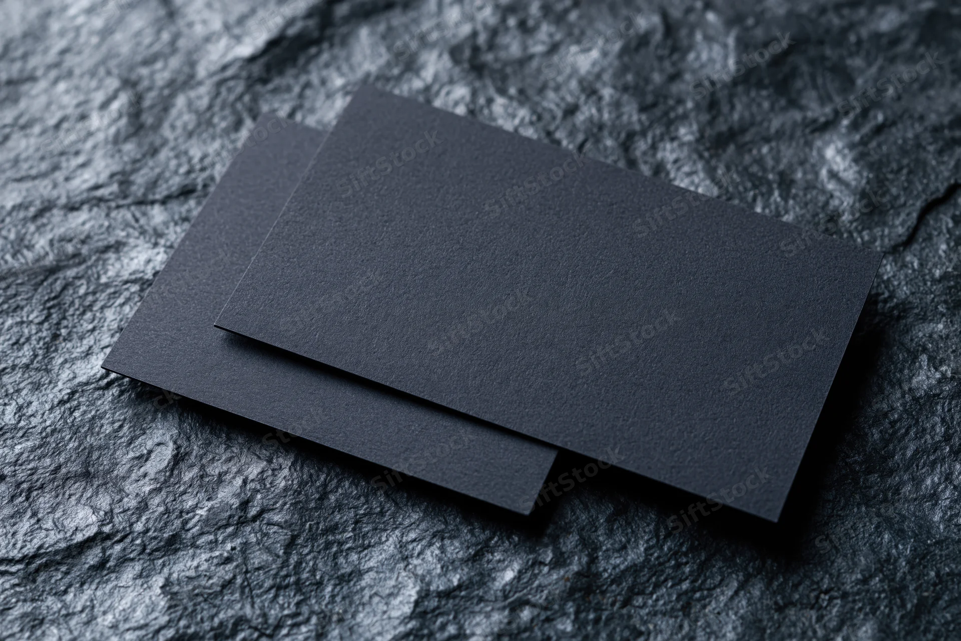 Two blank dark navy business cards overlapping on a textured stone surface