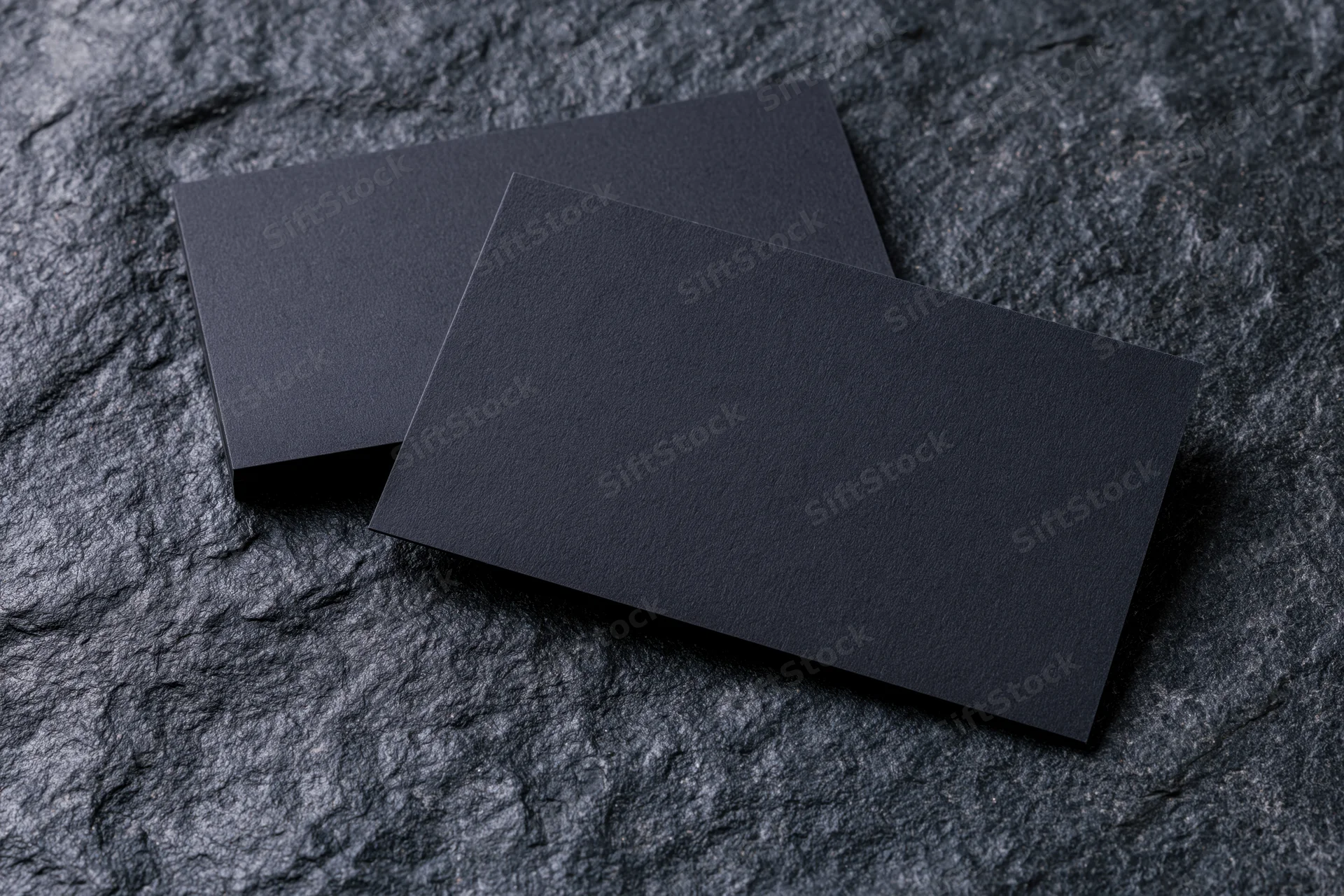 Two blank dark navy business cards resting on a textured slate surface