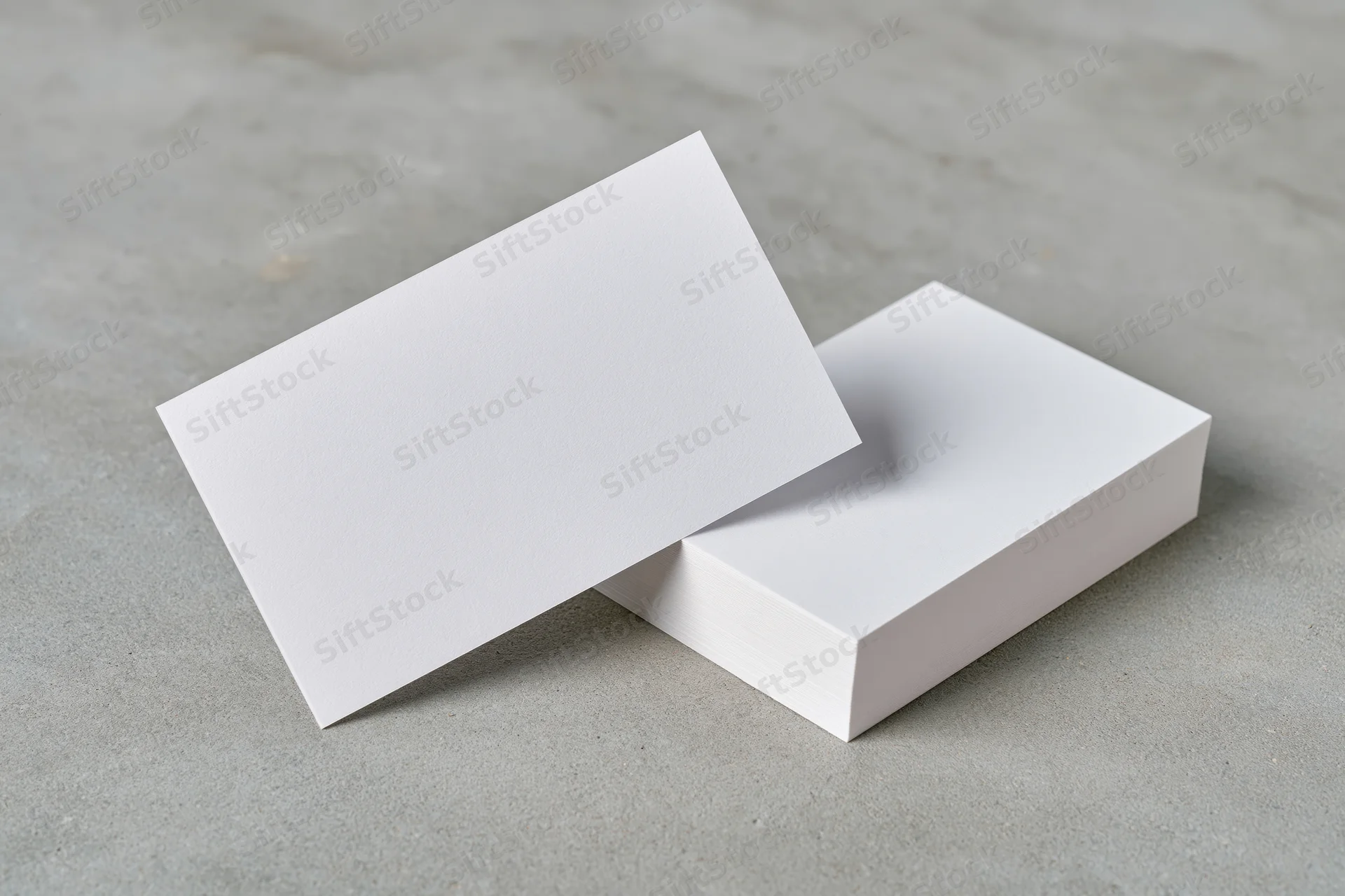 Blank white business cards arranged on a light grey concrete surface