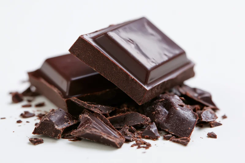 Dark chocolate squares stacked with broken pieces on white background