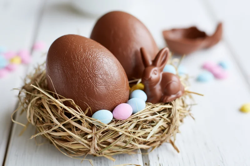 Chocolate easter eggs and bunny in straw nest on white wooden surface
