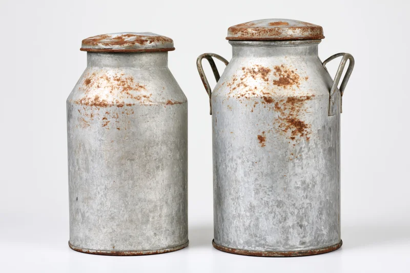 Two old metal milk cans standing side by side on white background