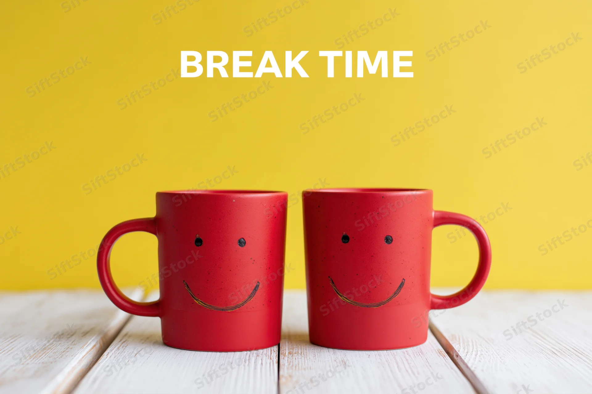 Two red ceramic coffee mugs with hand-drawn smiley faces on a white wooden table against a yellow background