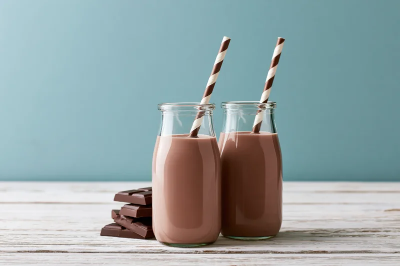 Two glass bottles of chocolate milk with striped straws on a wooden table